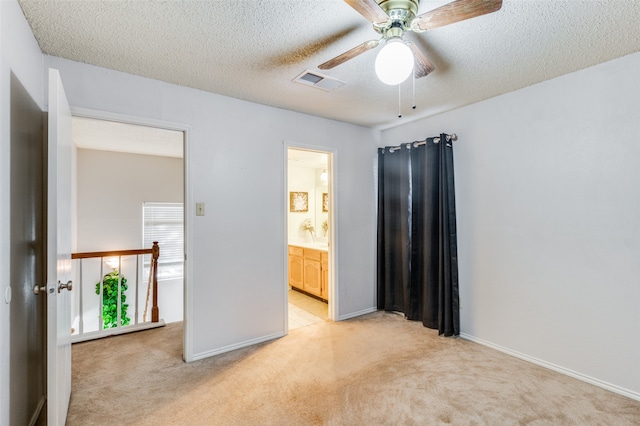 unfurnished bedroom featuring a textured ceiling, ceiling fan, light carpet, and ensuite bath