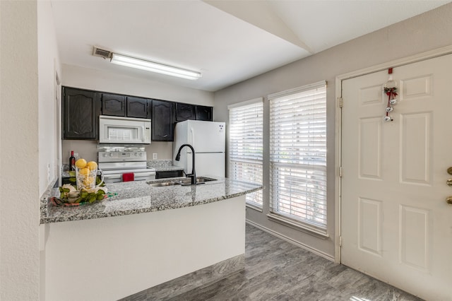 kitchen featuring kitchen peninsula, light stone counters, white appliances, sink, and hardwood / wood-style floors