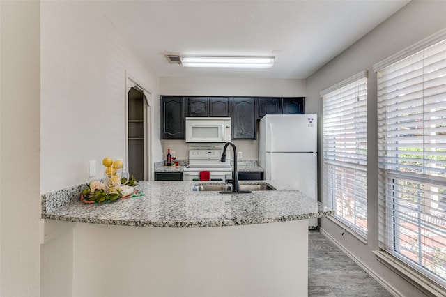 kitchen featuring kitchen peninsula, light stone counters, sink, and white appliances