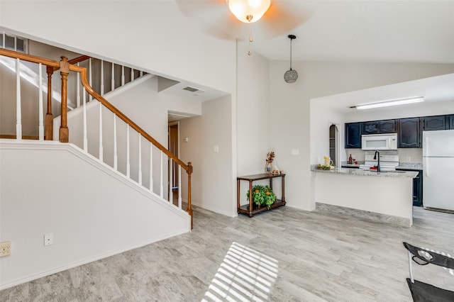 interior space featuring light stone counters, kitchen peninsula, light hardwood / wood-style floors, decorative light fixtures, and white appliances