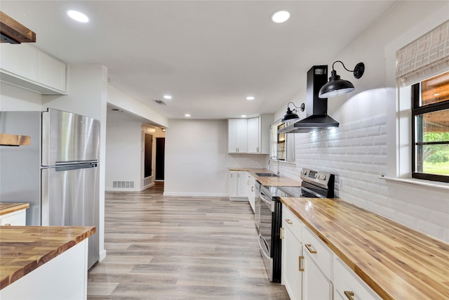 kitchen with appliances with stainless steel finishes, white cabinetry, range hood, light hardwood / wood-style floors, and butcher block countertops