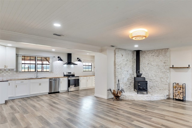 unfurnished living room with light hardwood / wood-style floors, a healthy amount of sunlight, a wood stove, and ornamental molding