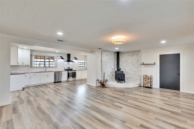 unfurnished living room featuring crown molding, a wood stove, sink, and light wood-type flooring