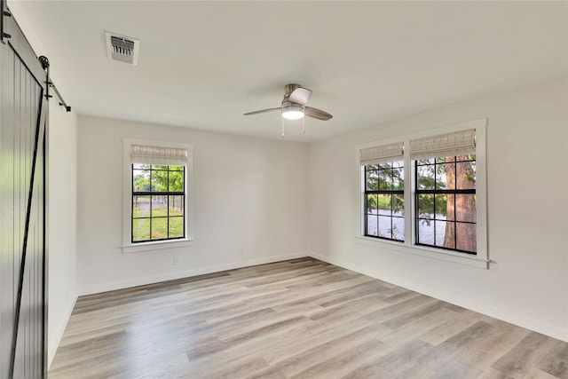 spare room featuring light hardwood / wood-style flooring, a barn door, and ceiling fan