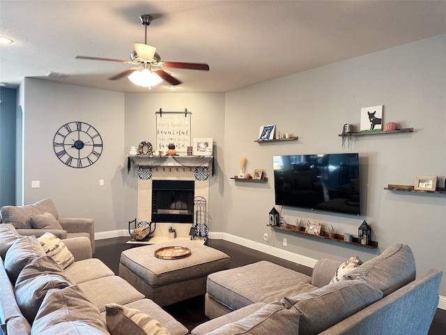 living room with dark wood-type flooring, a tiled fireplace, and ceiling fan