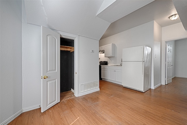 kitchen featuring vaulted ceiling, white cabinetry, white fridge, a textured ceiling, and light hardwood / wood-style floors