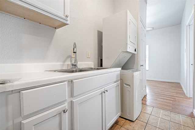 laundry area featuring cabinets, light hardwood / wood-style flooring, stacked washer / drying machine, and sink