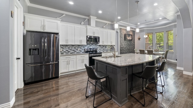 kitchen featuring white cabinets, a kitchen island with sink, light stone countertops, dark wood-type flooring, and stainless steel appliances