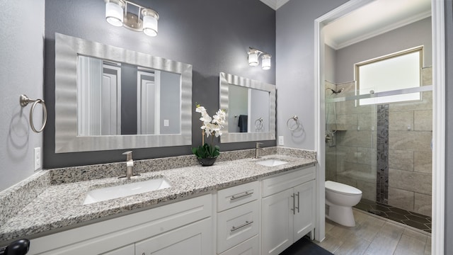 bathroom with tiled shower, toilet, wood-type flooring, ornamental molding, and vanity