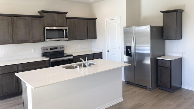 kitchen featuring a kitchen island with sink, sink, dark brown cabinets, light hardwood / wood-style floors, and stainless steel appliances