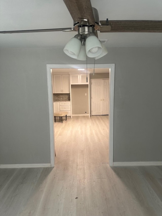 interior space featuring baseboards, ceiling fan, light wood-style flooring, and visible vents