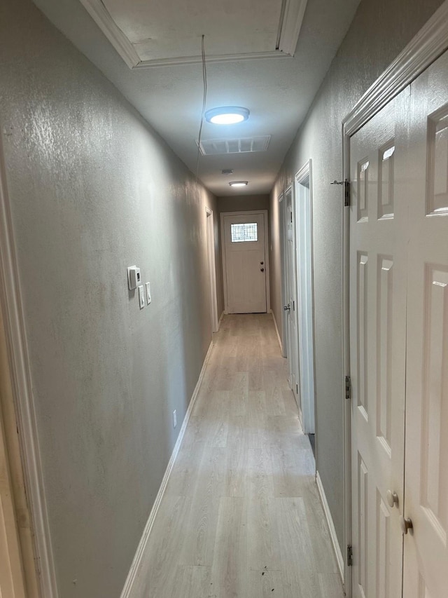 hallway with baseboards, visible vents, a textured wall, and light wood finished floors