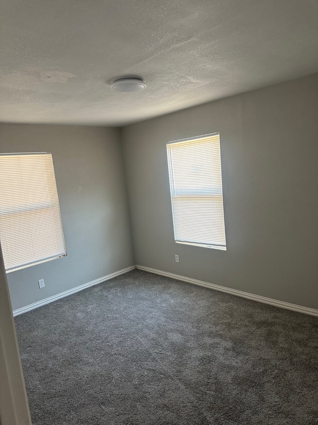 unfurnished room featuring a textured ceiling and dark carpet