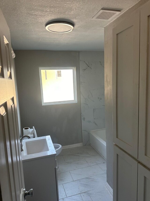 full bath with toilet, a textured ceiling, marble finish floor, and vanity