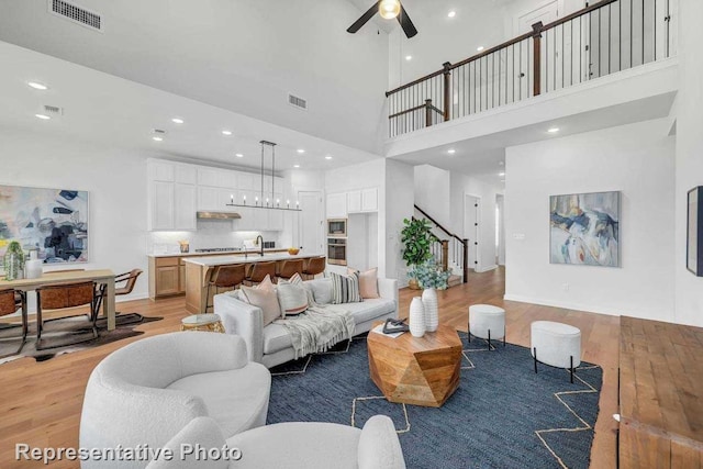 living room with ceiling fan, a high ceiling, and light wood-type flooring