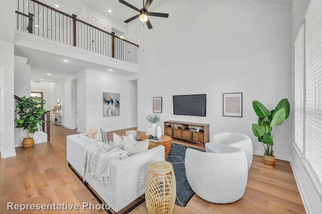 living room with a towering ceiling, light wood-type flooring, and ceiling fan