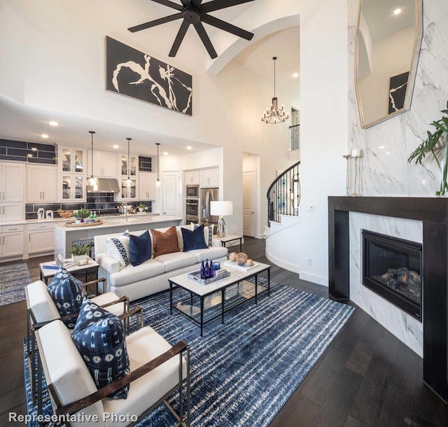 living room featuring a premium fireplace, a high ceiling, ceiling fan with notable chandelier, and dark hardwood / wood-style flooring