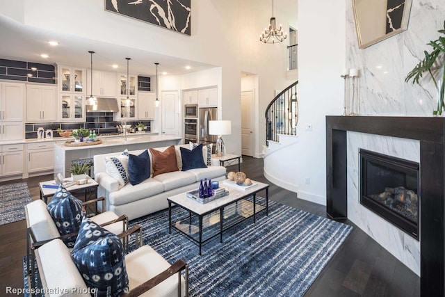 living room featuring dark wood-type flooring, a notable chandelier, a high ceiling, and a high end fireplace