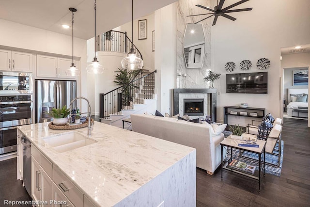 kitchen featuring a high ceiling, stainless steel appliances, a center island with sink, sink, and decorative light fixtures