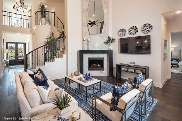 living room with a fireplace, french doors, a high ceiling, dark wood-type flooring, and an inviting chandelier