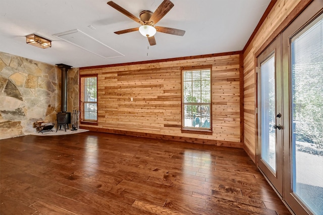 unfurnished living room with ceiling fan, wood walls, a wood stove, and dark hardwood / wood-style floors