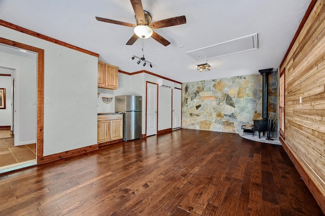 unfurnished living room with a wall unit AC, ceiling fan, hardwood / wood-style flooring, ornamental molding, and a wood stove