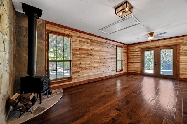 unfurnished living room with french doors, wooden walls, wood-type flooring, a wood stove, and ceiling fan