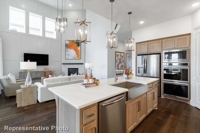 kitchen with appliances with stainless steel finishes, an island with sink, a fireplace, and hanging light fixtures