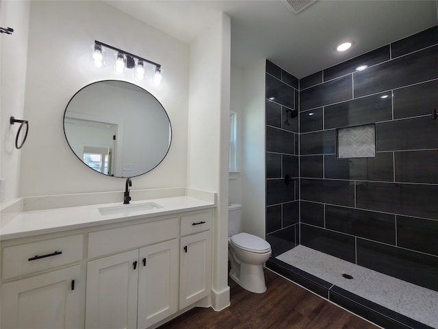 bathroom with vanity, toilet, wood-type flooring, and a tile shower