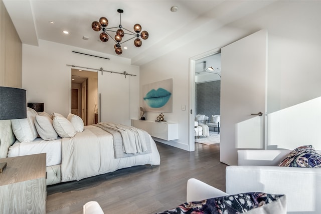 bedroom featuring a barn door, dark hardwood / wood-style floors, an inviting chandelier, and ensuite bath