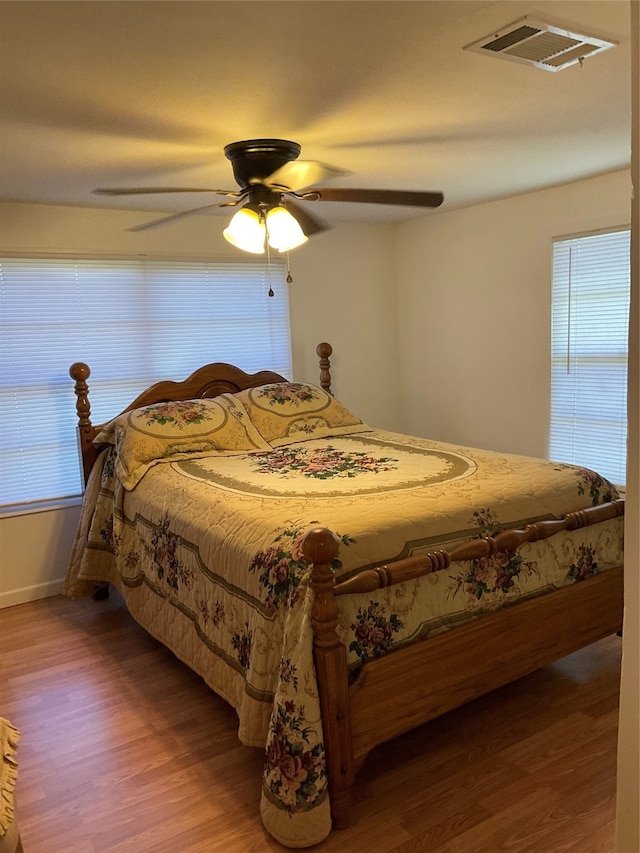 bedroom featuring ceiling fan, hardwood / wood-style flooring, and multiple windows