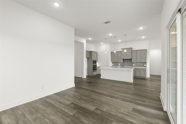 kitchen featuring decorative backsplash, dark hardwood / wood-style flooring, a kitchen island with sink, pendant lighting, and gray cabinets