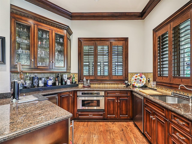 kitchen with appliances with stainless steel finishes, sink, light hardwood / wood-style floors, dark stone countertops, and crown molding