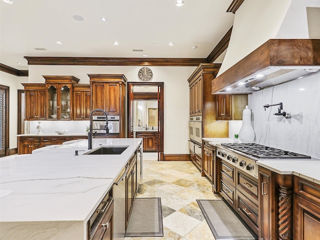 kitchen with an island with sink, ornamental molding, sink, premium range hood, and appliances with stainless steel finishes