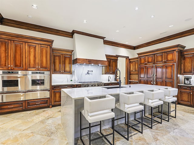 kitchen with a large island with sink, appliances with stainless steel finishes, sink, custom range hood, and a breakfast bar