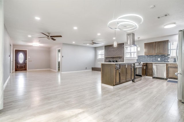 kitchen featuring island exhaust hood, hanging light fixtures, ceiling fan, appliances with stainless steel finishes, and light hardwood / wood-style flooring