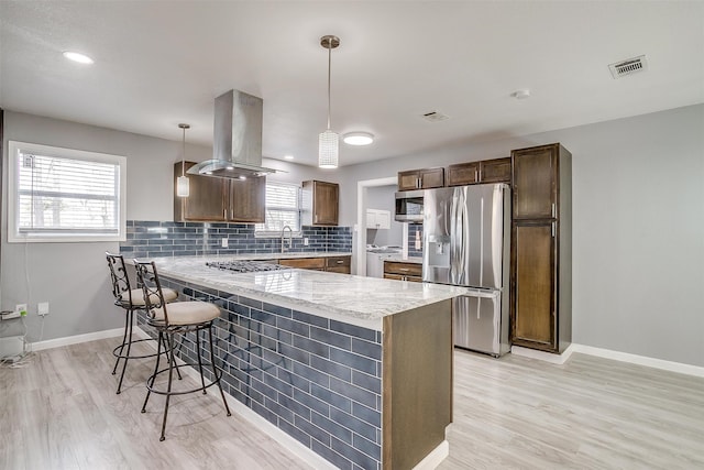 kitchen with island exhaust hood, stainless steel appliances, hanging light fixtures, and a wealth of natural light