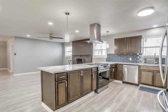 kitchen with island range hood, light hardwood / wood-style flooring, hanging light fixtures, a brick fireplace, and appliances with stainless steel finishes