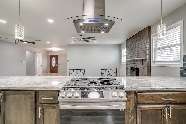 kitchen featuring stainless steel range with gas stovetop, island exhaust hood, light stone countertops, and pendant lighting