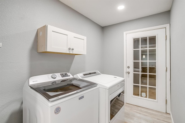 clothes washing area with washer and clothes dryer, light hardwood / wood-style flooring, and cabinets