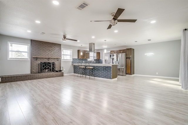 unfurnished living room featuring sink, a brick fireplace, light wood-type flooring, and ceiling fan