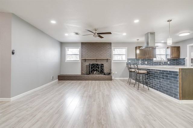 unfurnished living room featuring light hardwood / wood-style floors, sink, a fireplace, and ceiling fan