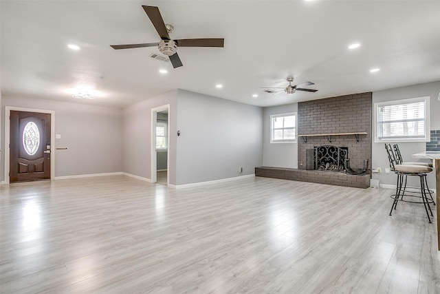 unfurnished living room featuring ceiling fan, a healthy amount of sunlight, a brick fireplace, and light wood-type flooring