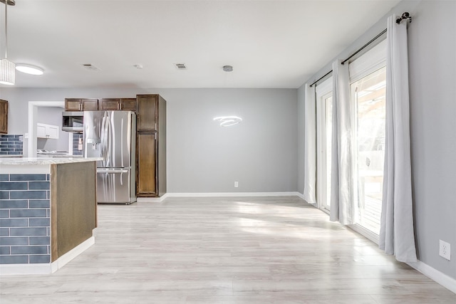 kitchen with appliances with stainless steel finishes, hanging light fixtures, light wood-type flooring, and tasteful backsplash