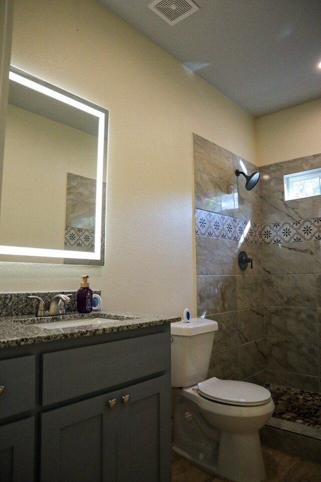 bathroom featuring vanity, toilet, wood-type flooring, and tiled shower