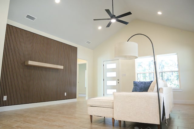 living room featuring ceiling fan, high vaulted ceiling, and wood walls