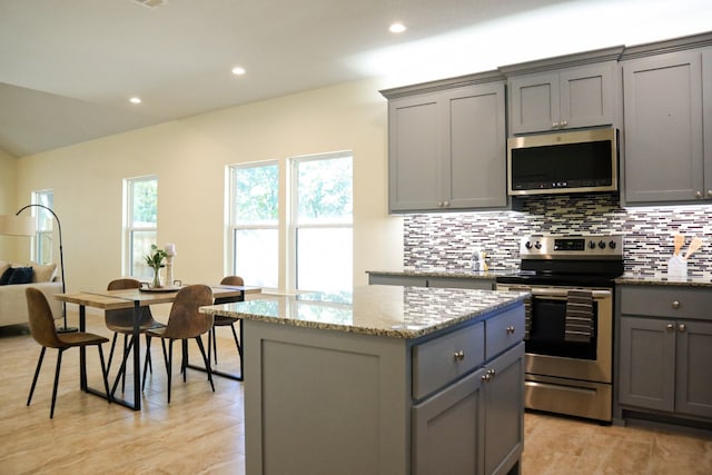 kitchen with light stone countertops, appliances with stainless steel finishes, a kitchen island, backsplash, and gray cabinets