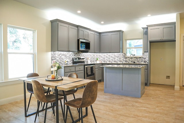 kitchen featuring decorative backsplash, a kitchen island, appliances with stainless steel finishes, light hardwood / wood-style flooring, and gray cabinetry