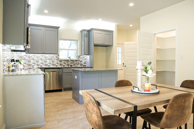 kitchen featuring dishwasher, light stone countertops, a kitchen island, and gray cabinetry