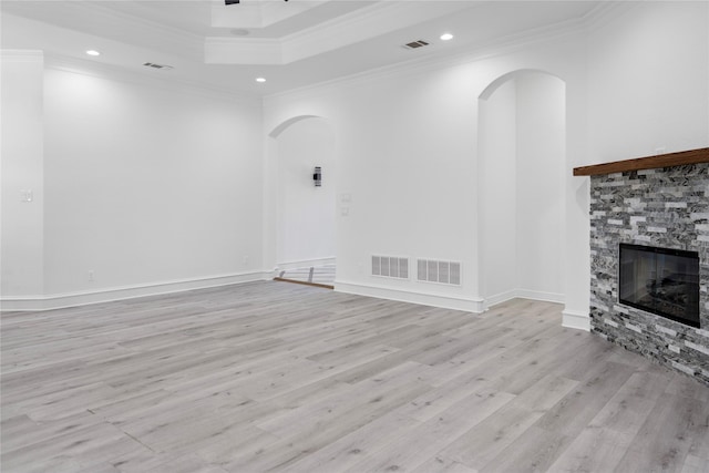 unfurnished living room with light hardwood / wood-style floors, a stone fireplace, a tray ceiling, and crown molding